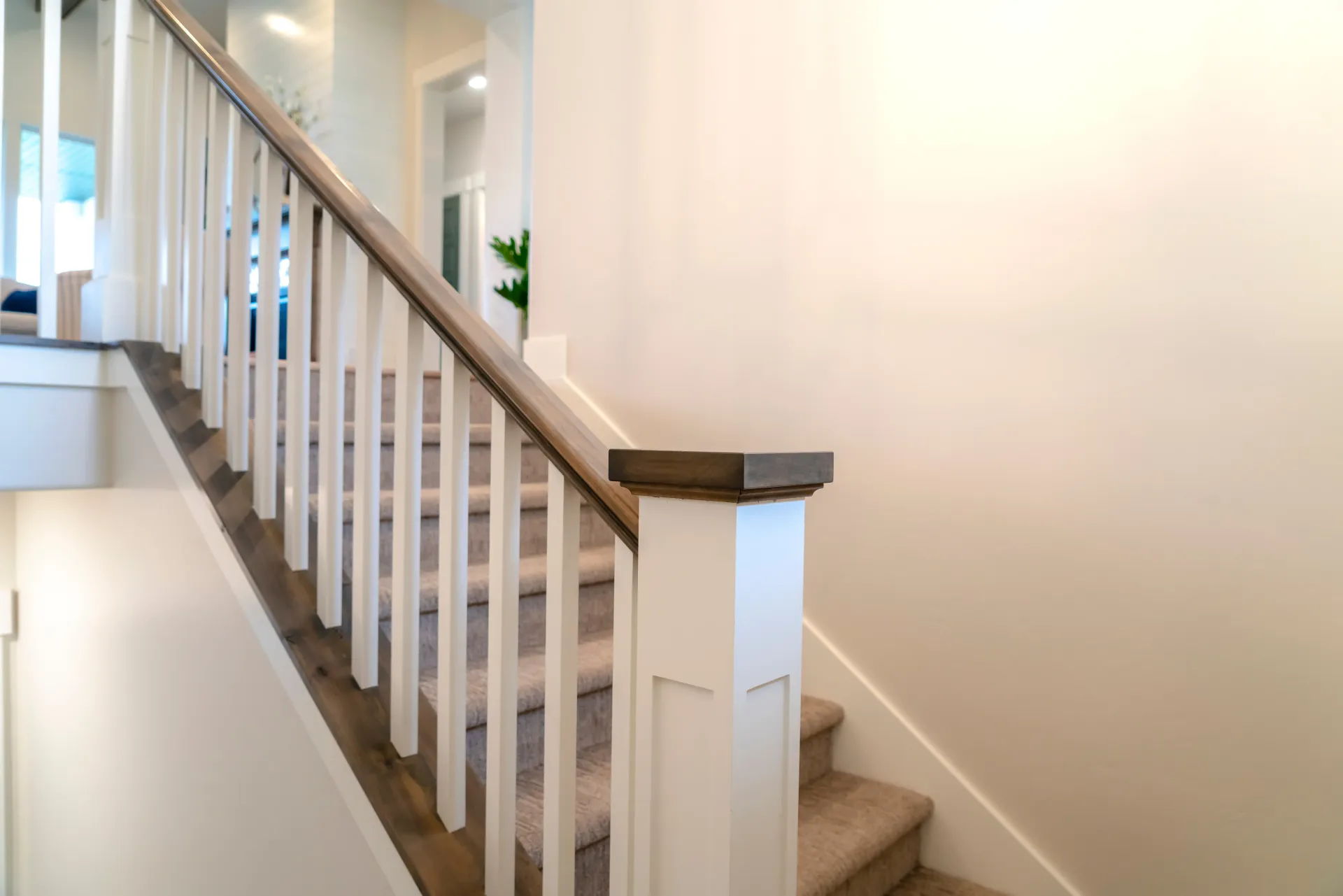 Staircase with white balusters, brown handrail, carpeted stairs, and a white pillar.