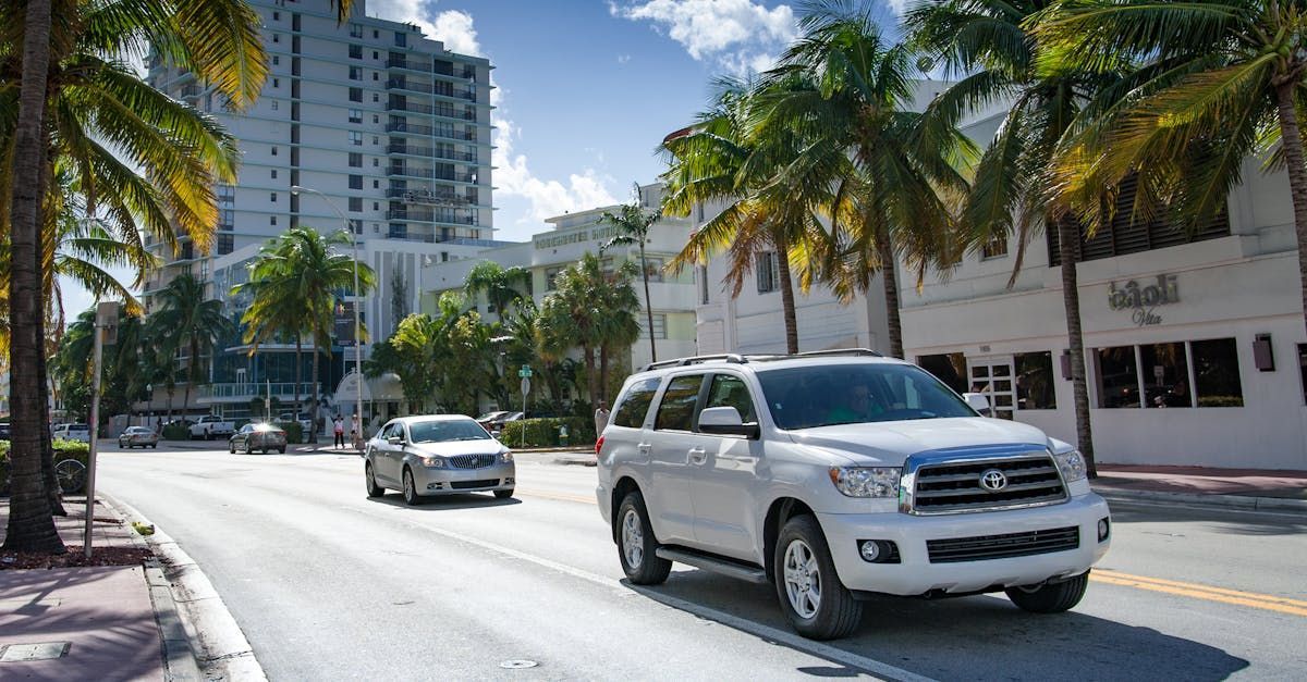 A white suv is driving down a city street next to palm trees.  | Chloe's Auto Repair and Tire