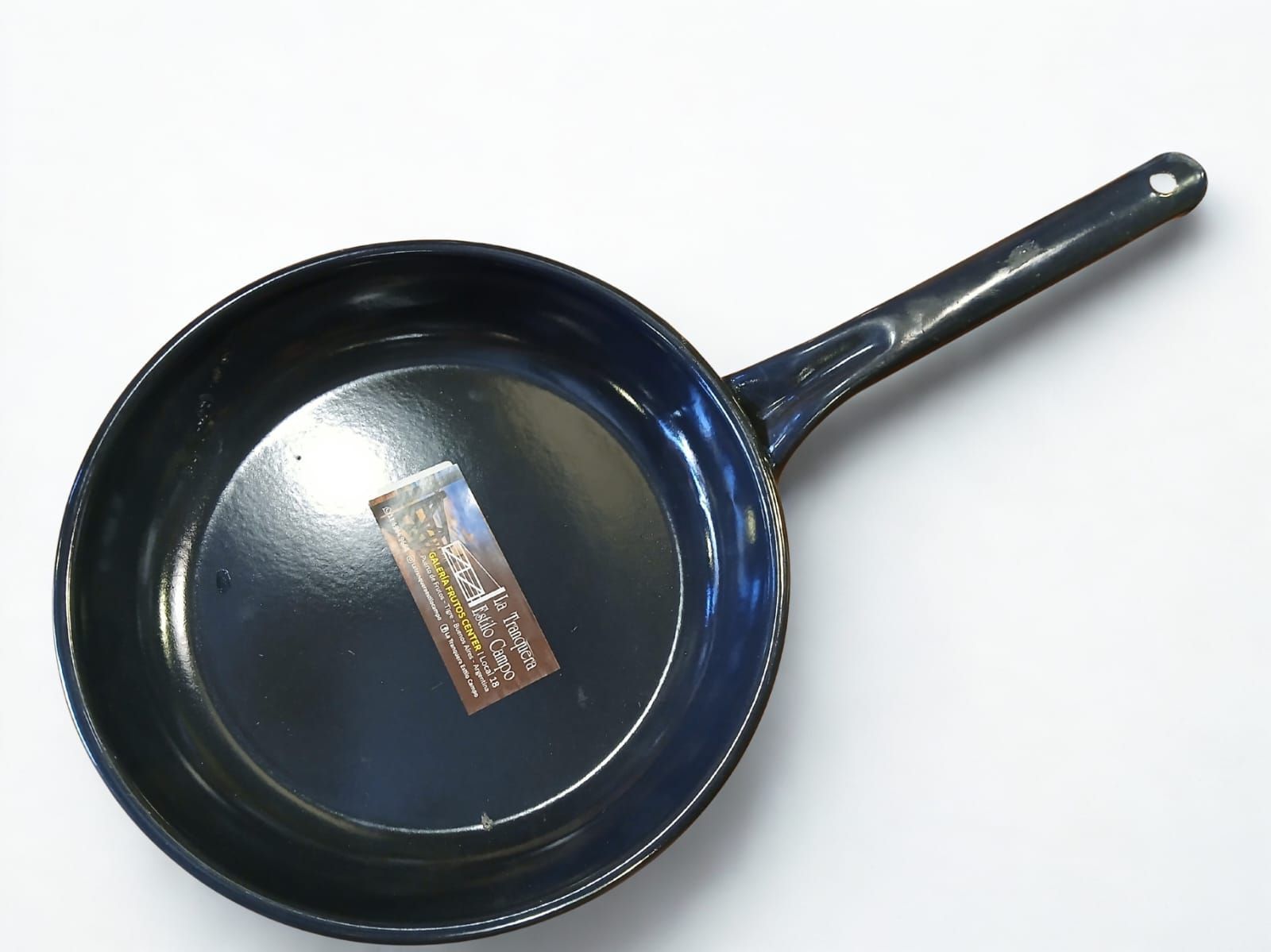 Sartén negra con mango largo sobre superficie blanca.