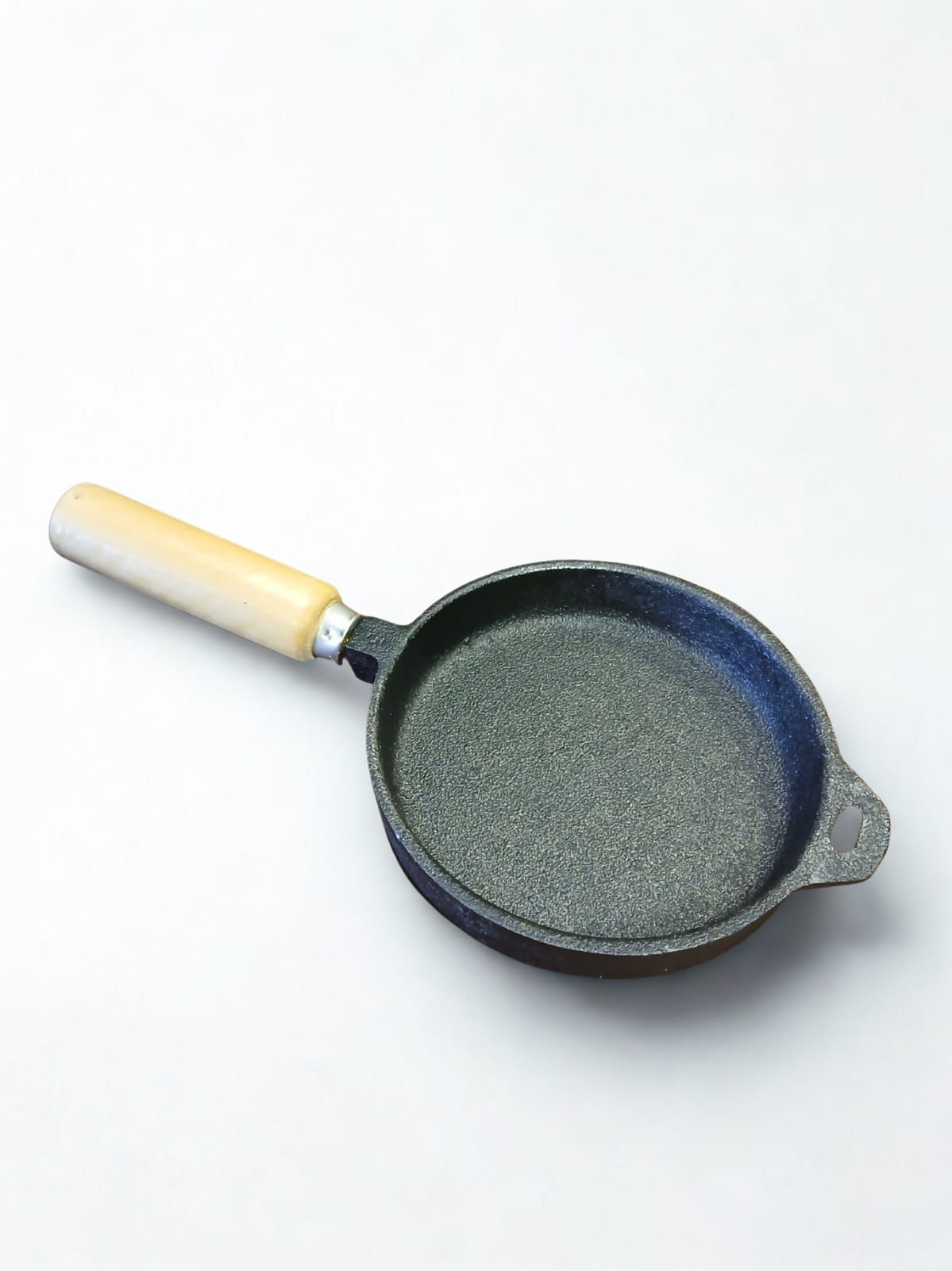 Sartén pequeña de color oscuro con mango de madera sobre una superficie blanca.