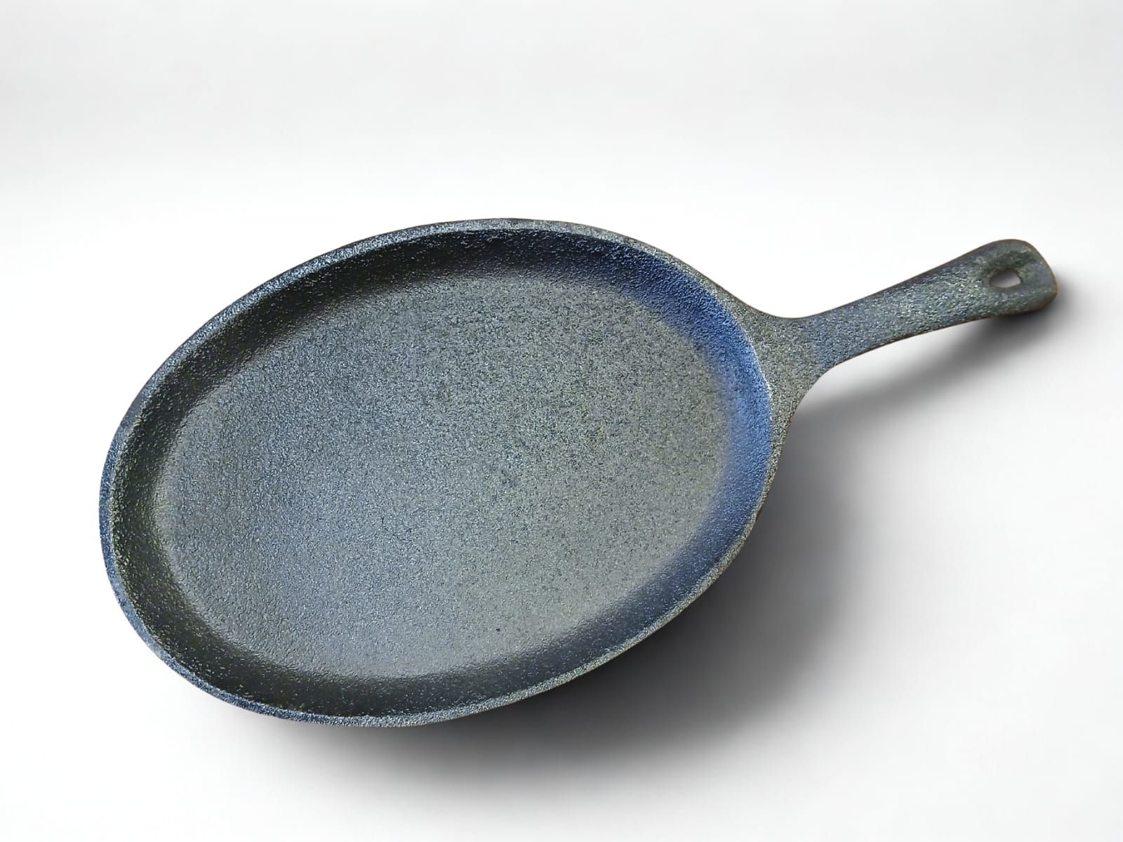 Sartén de hierro fundido azul grisáceo moteado, de forma ovalada, con mango y superficie blanca.