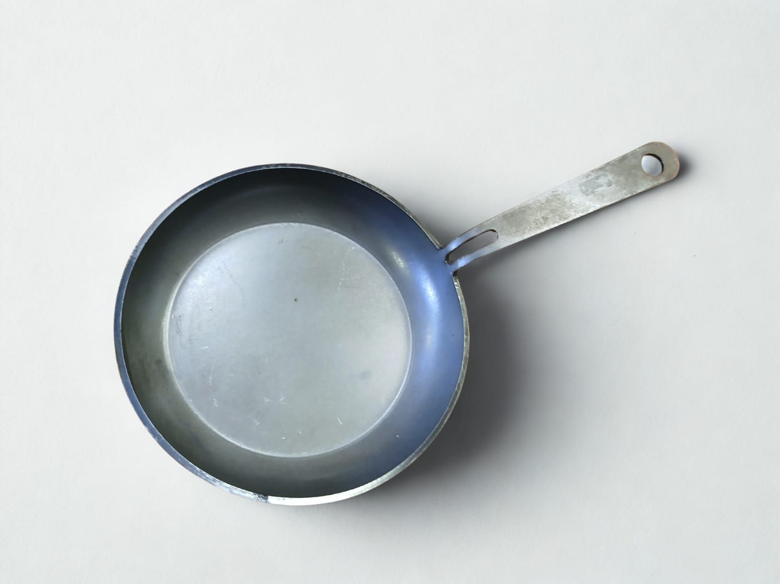 Sartén metálica pequeña, circular, con mango, colocada sobre una superficie gris.