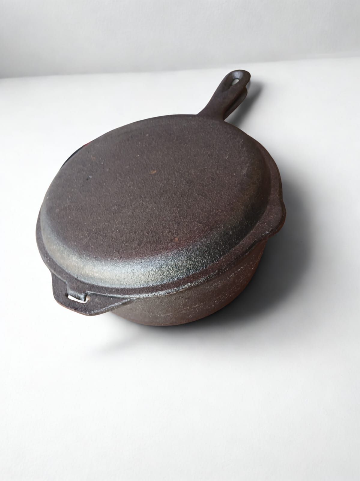 Sartén de hierro fundido sobre superficie blanca, con un pequeño mango en el lateral.
