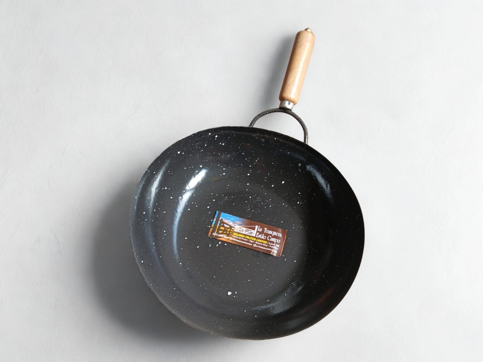 Wok moteado en negro con mango de madera sobre una superficie blanca.