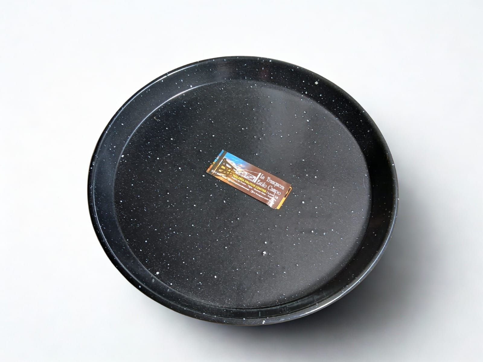 Bandeja moteada de color negro con un pequeño objeto rectangular colorido en el centro sobre un fondo blanco.