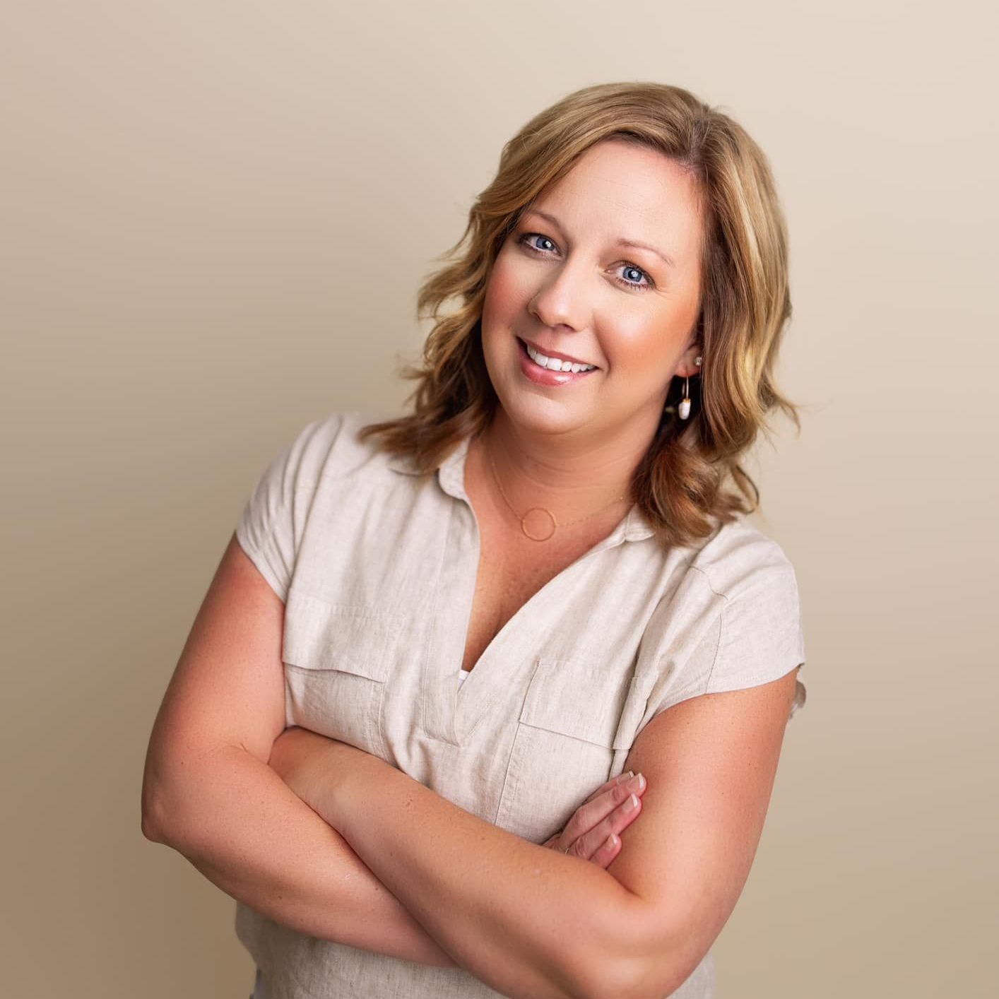 A woman wearing a white jacket and a brown shirt is smiling for the camera.