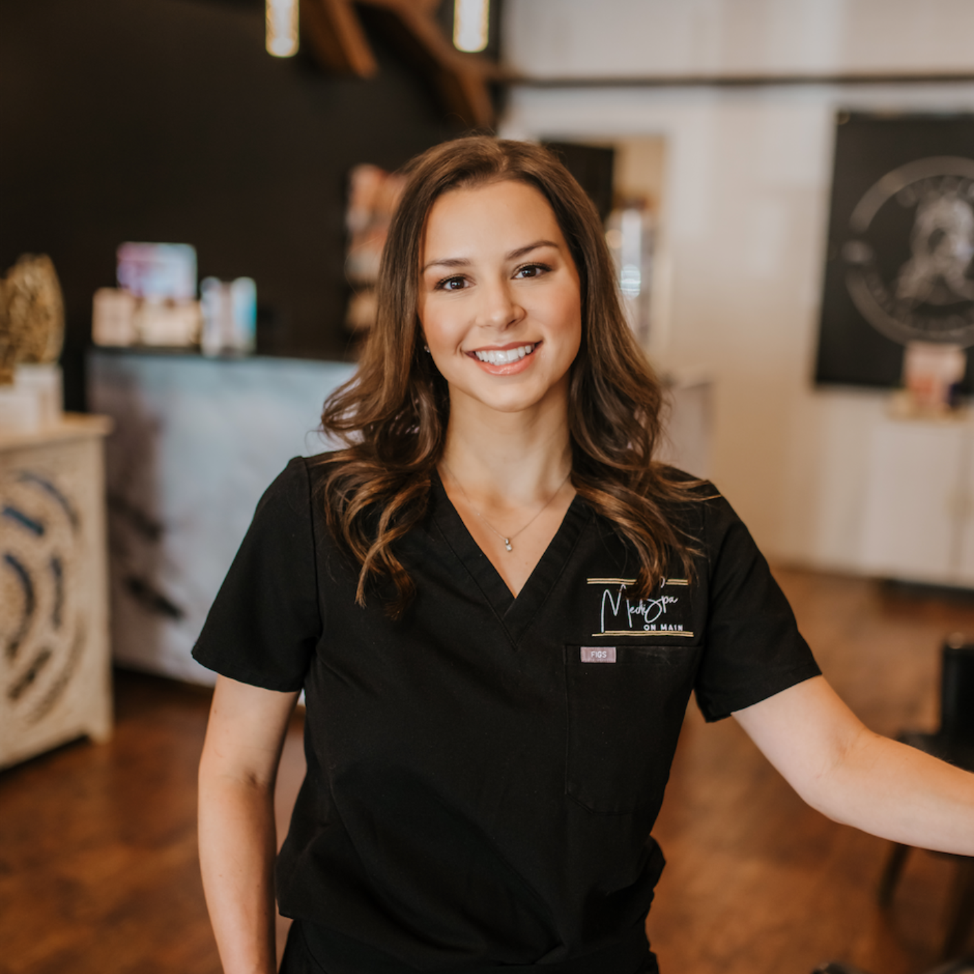 A woman wearing black scrubs is smiling for the camera at Medispa on main