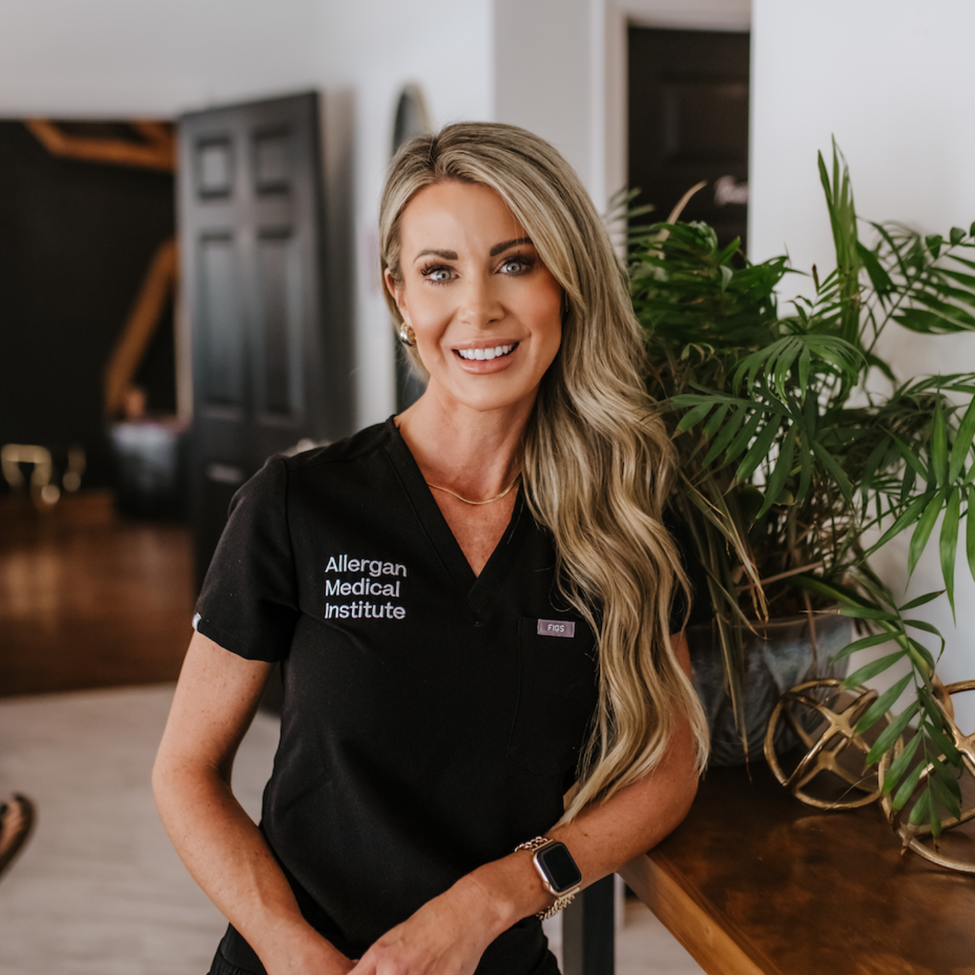 A woman wearing a set of black scrubs is smiling for the camera.