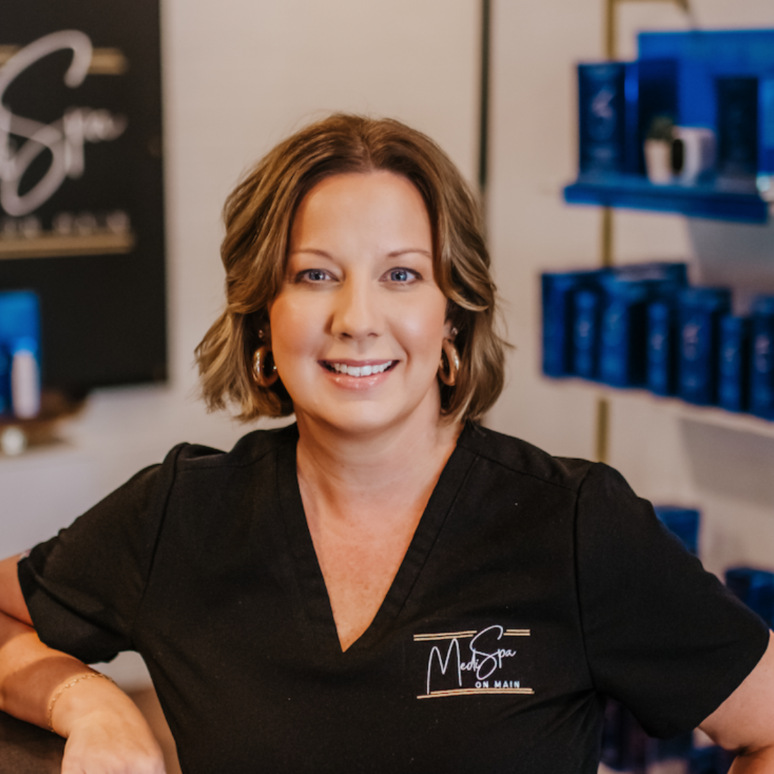 Woman smiling at the camera, wearing a black top, gold earrings, in a skincare clinic.