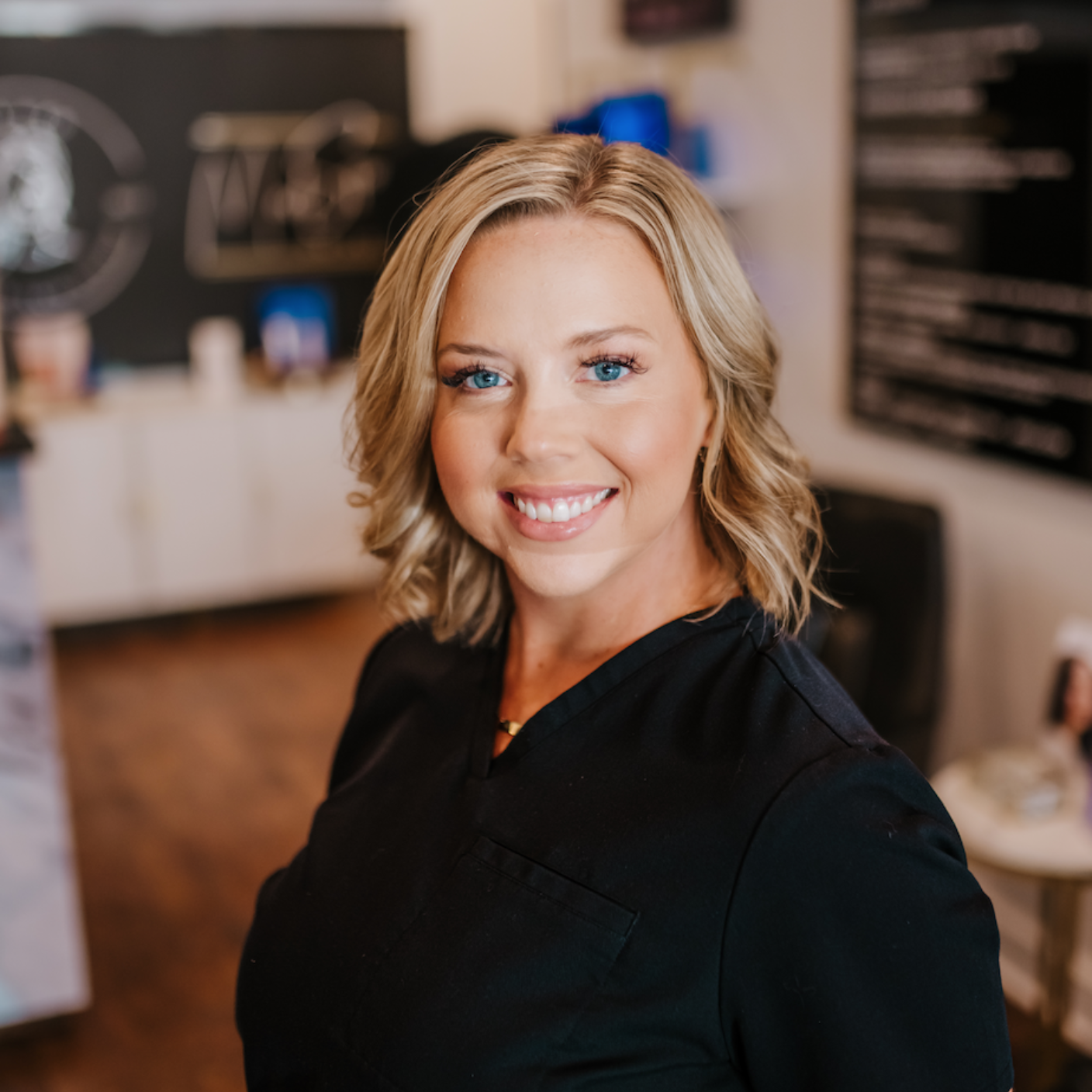 Blonde woman smiling at the camera, wearing a black top, in a shop setting.