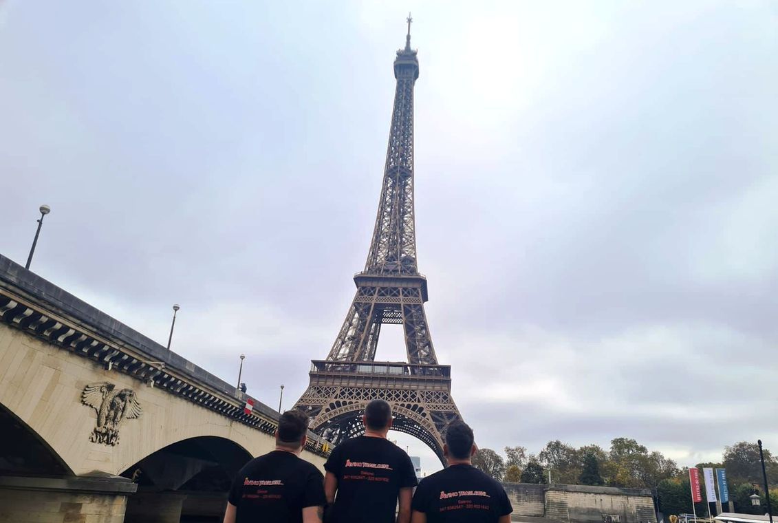 La Torre Eiffel a Parigi con tre persone in piedi in primo piano sotto un cielo nuvoloso.