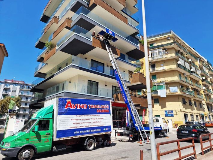 Camion per traslochi con scala parcheggiato davanti a un condominio in una via cittadina.