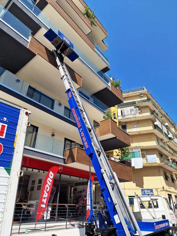 Ascensore mobile blu e bianco che raggiunge un balcone di un condominio cittadino.