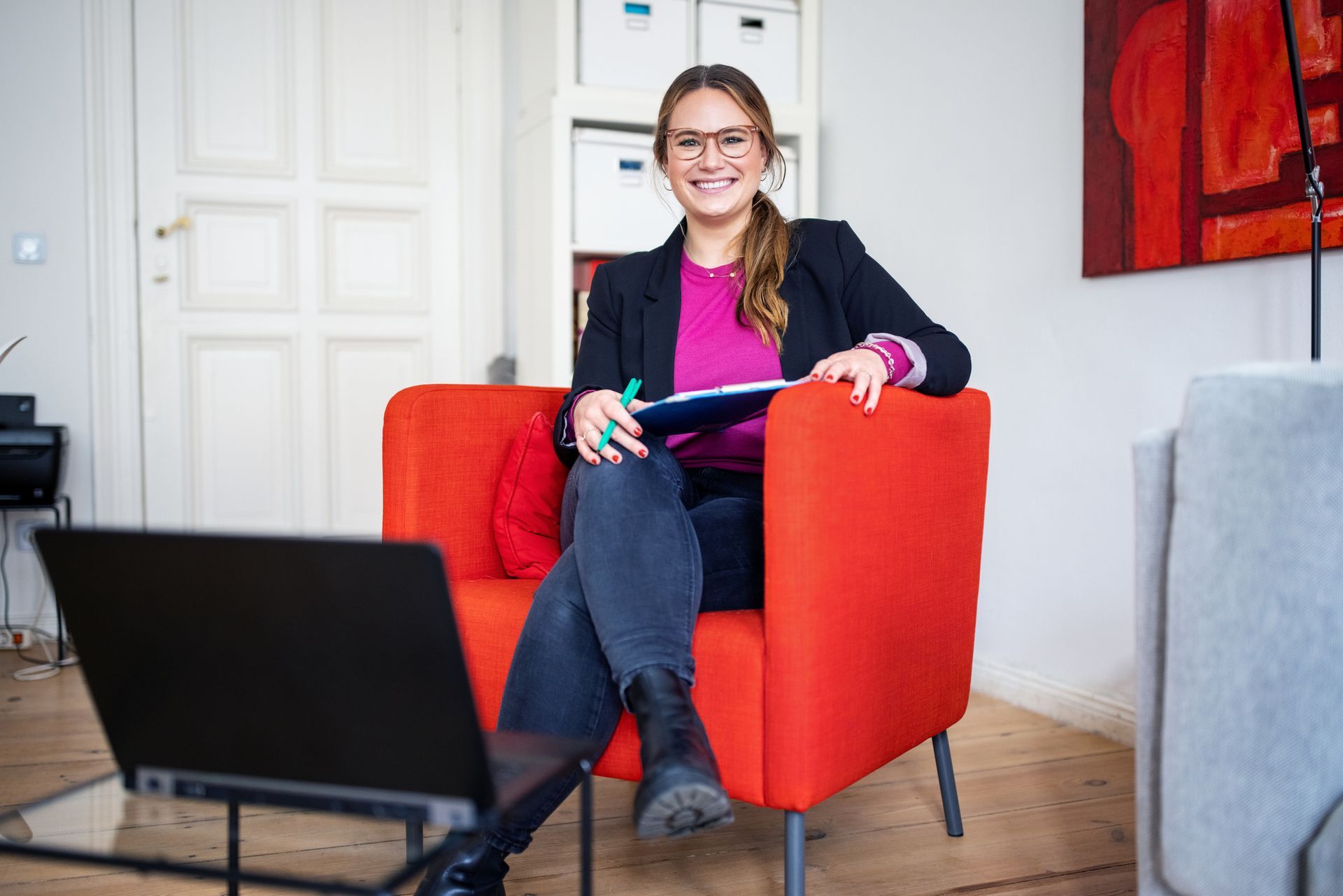 A woman is sitting in a red chair with a laptop.