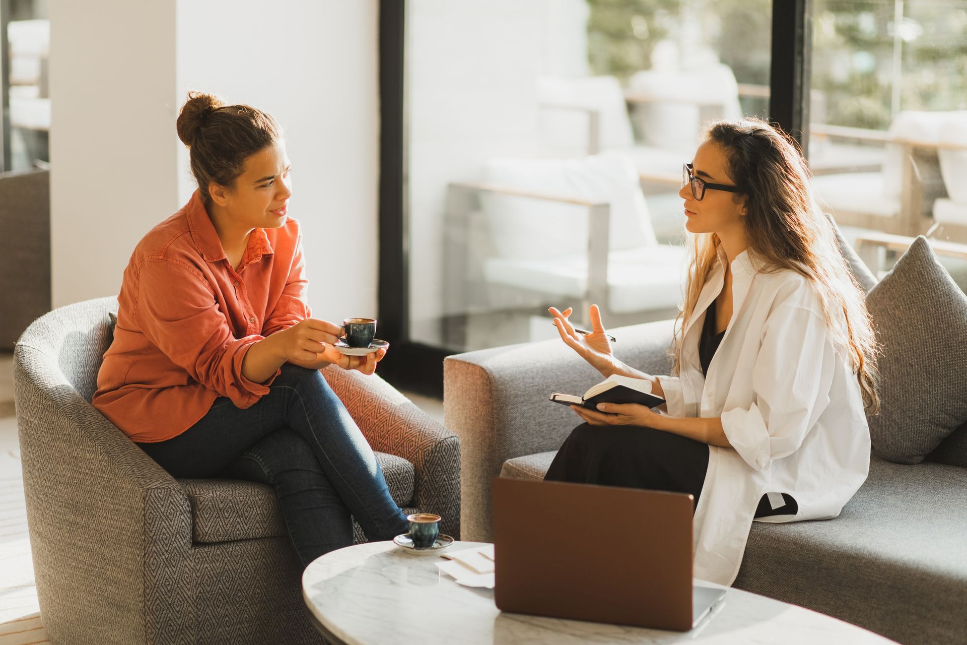 Two women are sitting on a couch talking to each other.
