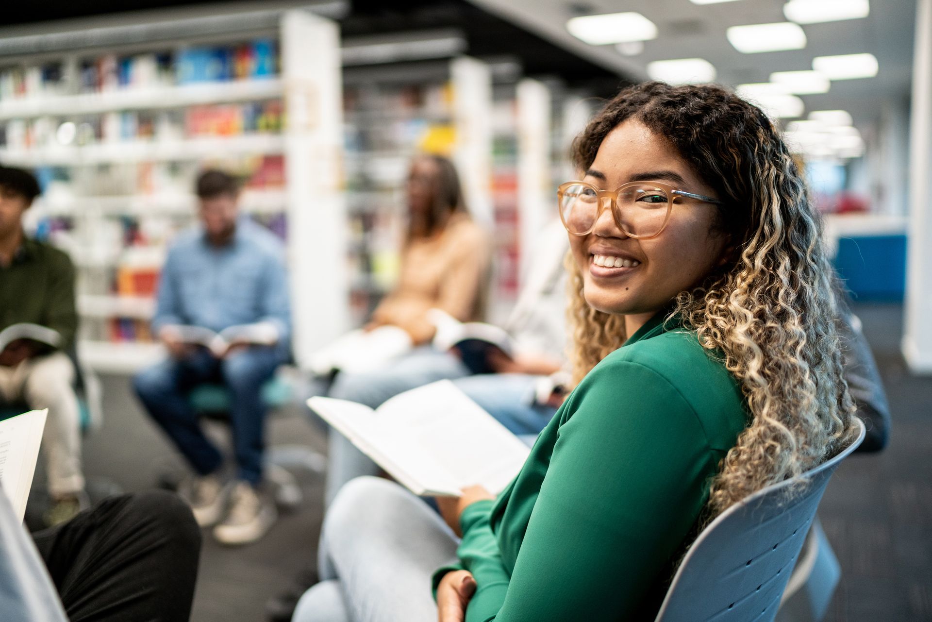 A woman is sitting in a chair in a library reading a book.