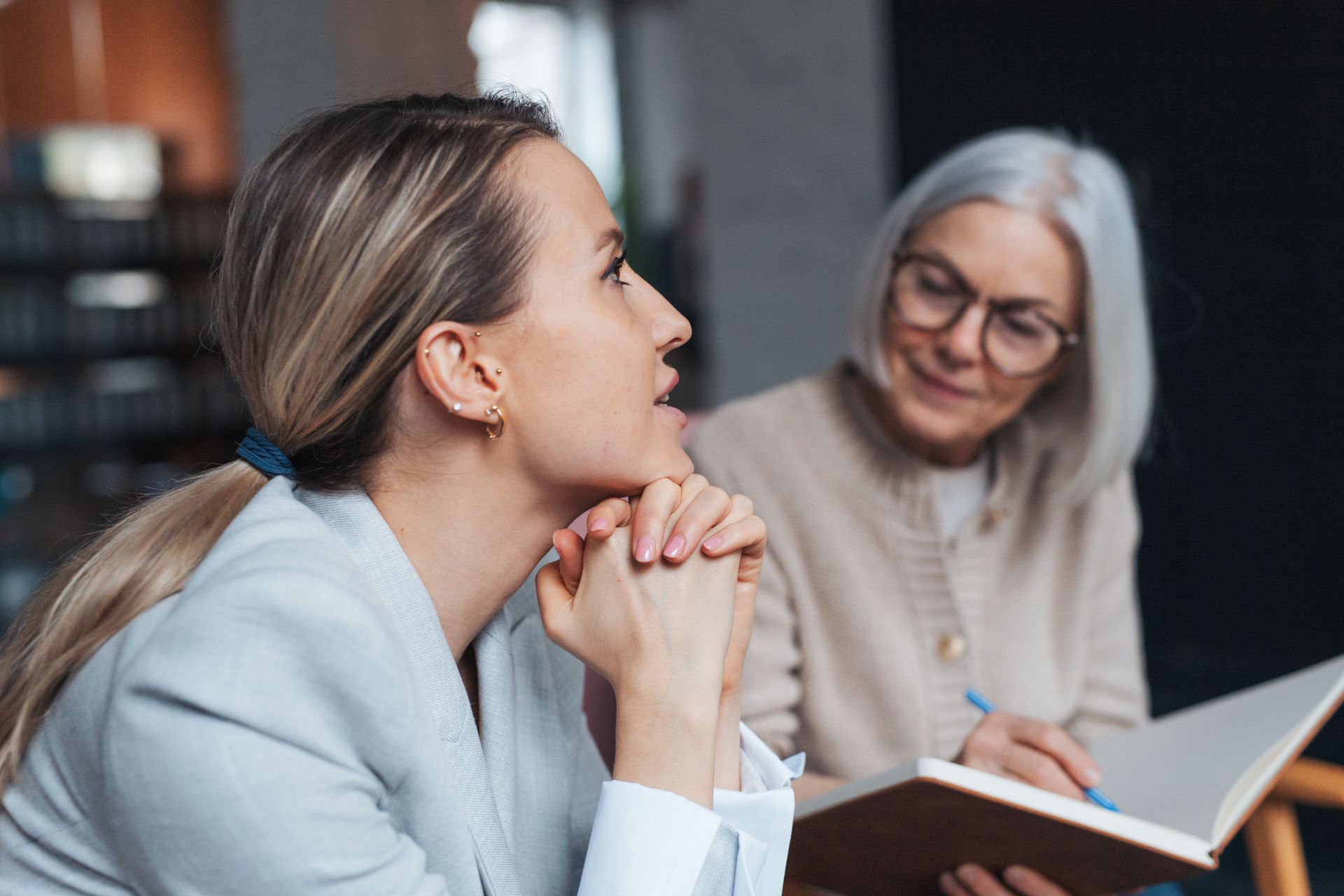 Two women are sitting at a table looking at a book.