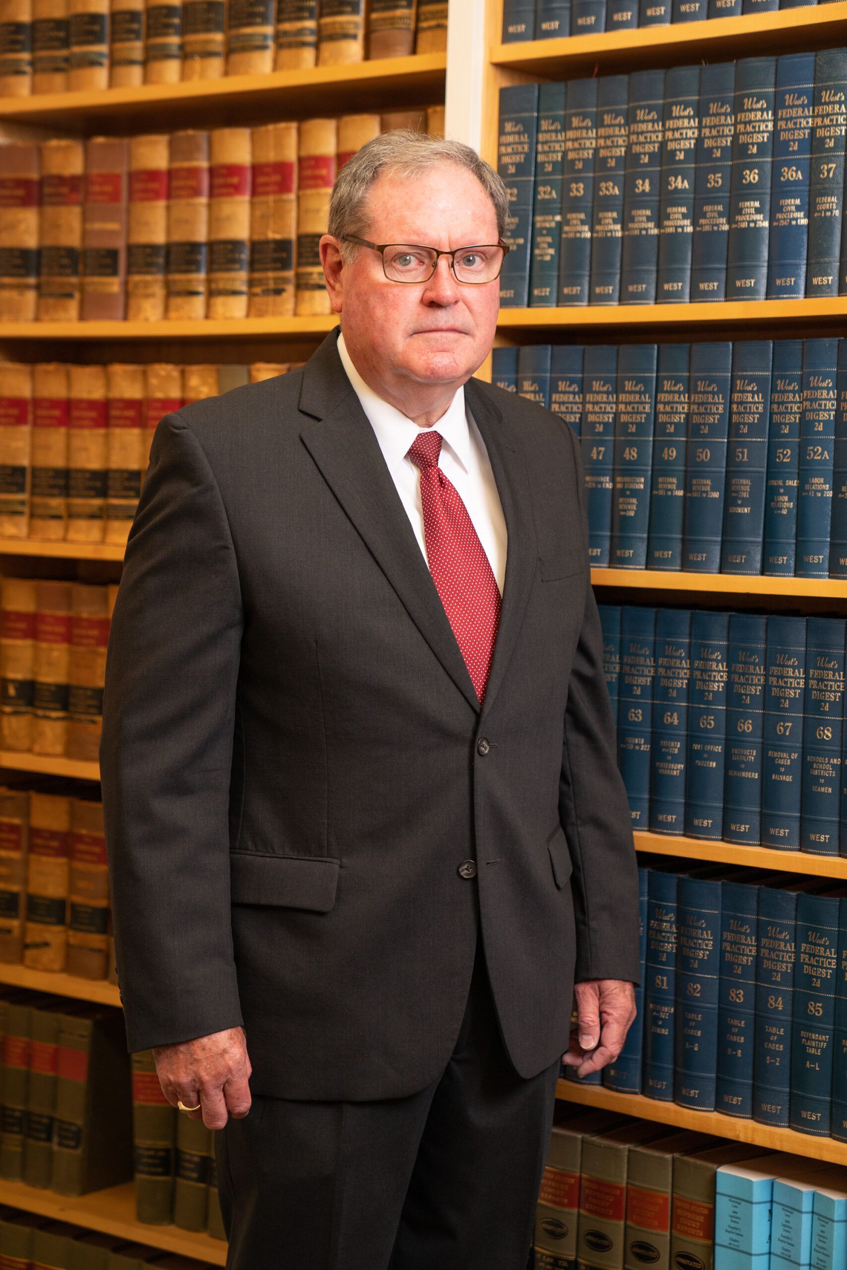 A person in a suit and red patterned tie stands in front of bookshelves filled with law books.