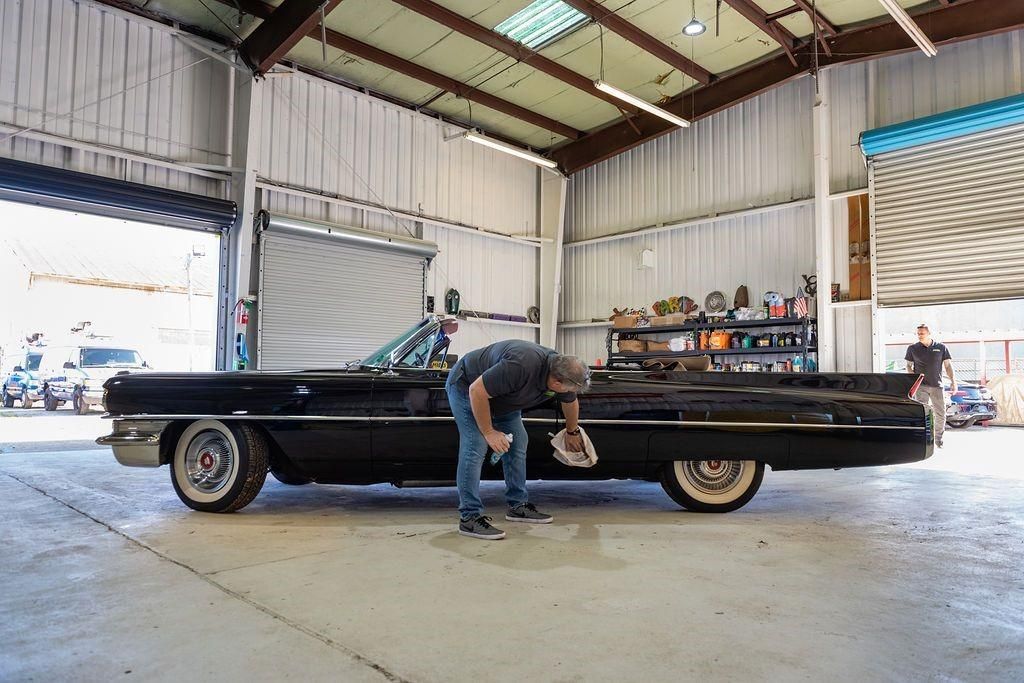 A man is standing next to a black car in a garage.