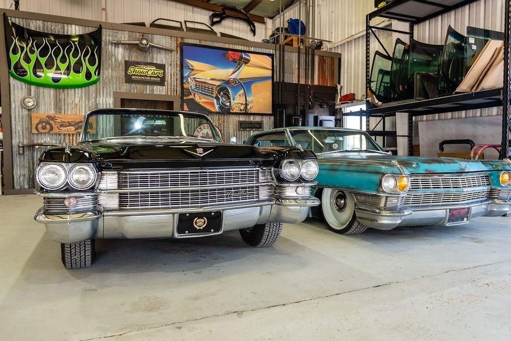 Two old cars are parked next to each other in a garage.