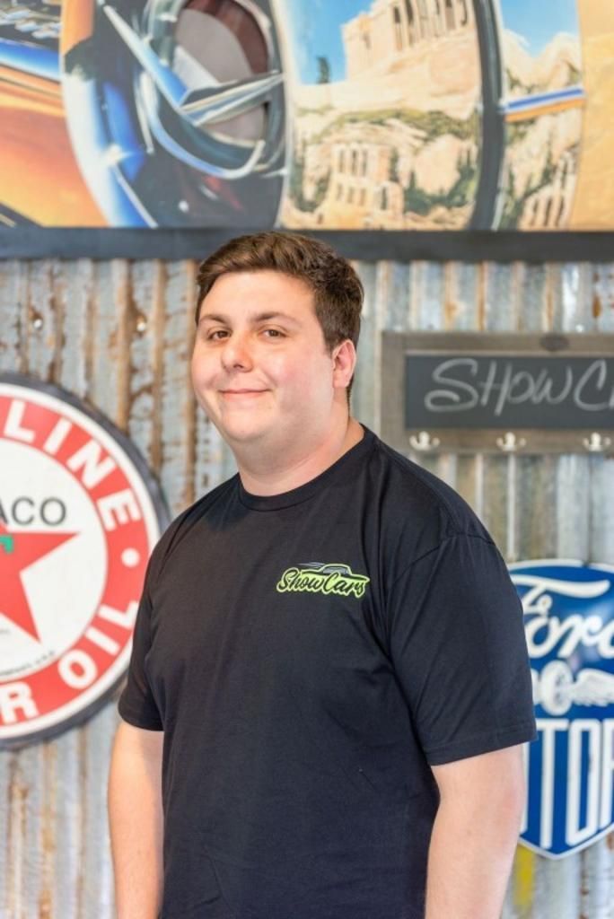 A man in a black shirt is standing in front of a wall with signs on it.