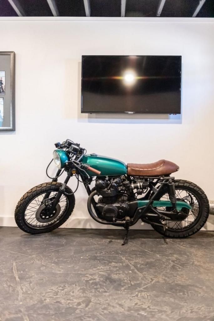 A green motorcycle is parked in a room next to a flat screen tv.