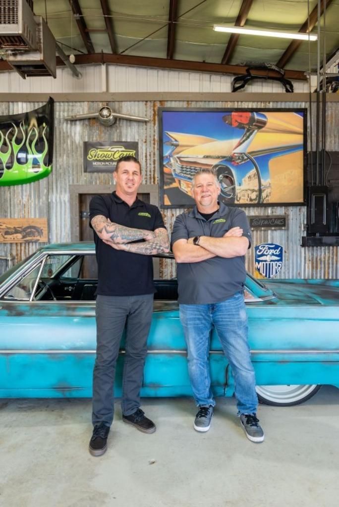 Two men are standing next to a car in a garage.