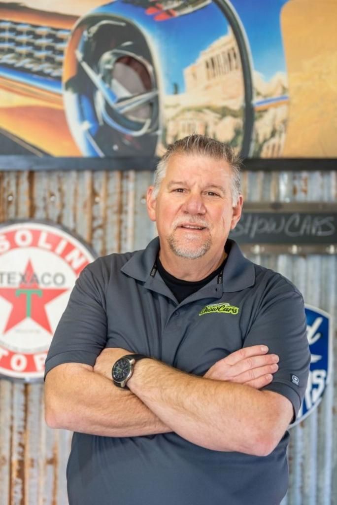 A man is standing with his arms crossed in front of a texaco sign.