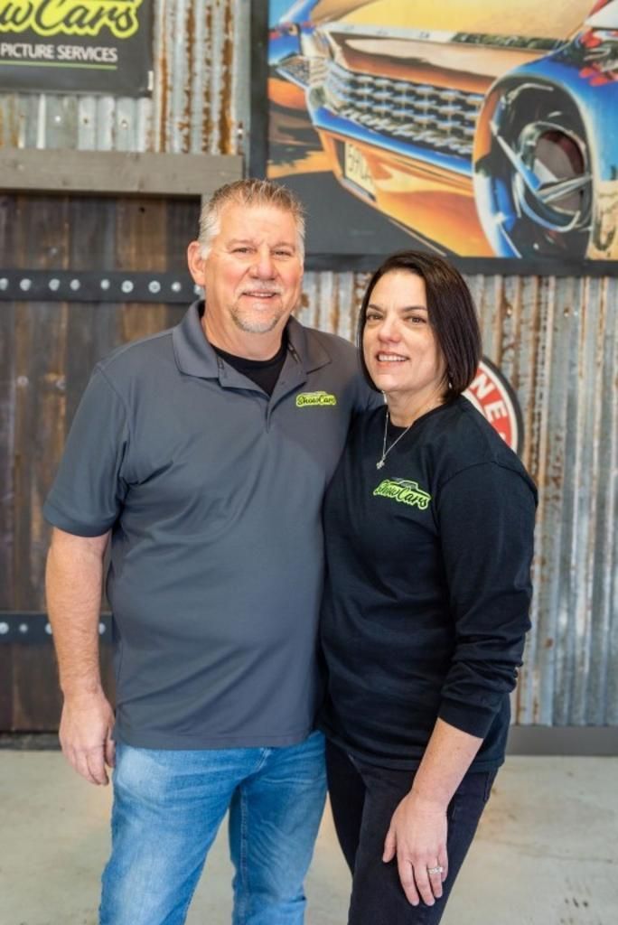 A man and a woman are posing for a picture in front of a car.