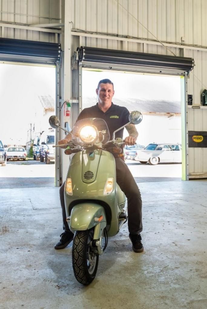 A man is sitting on a scooter in a garage.