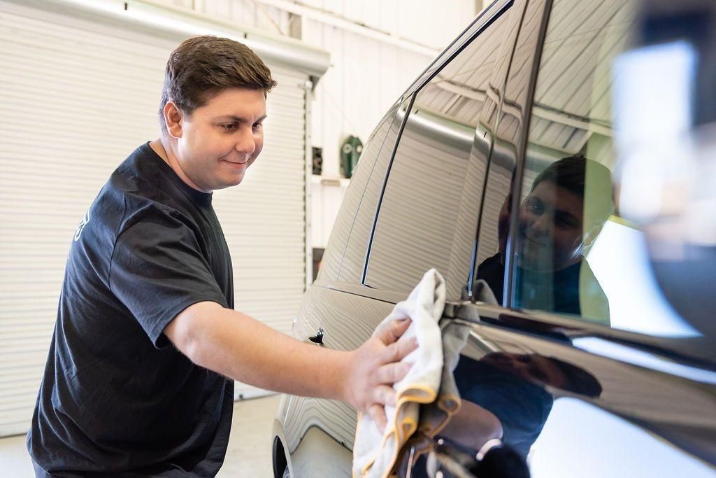 A man is cleaning a car with a towel in a garage.