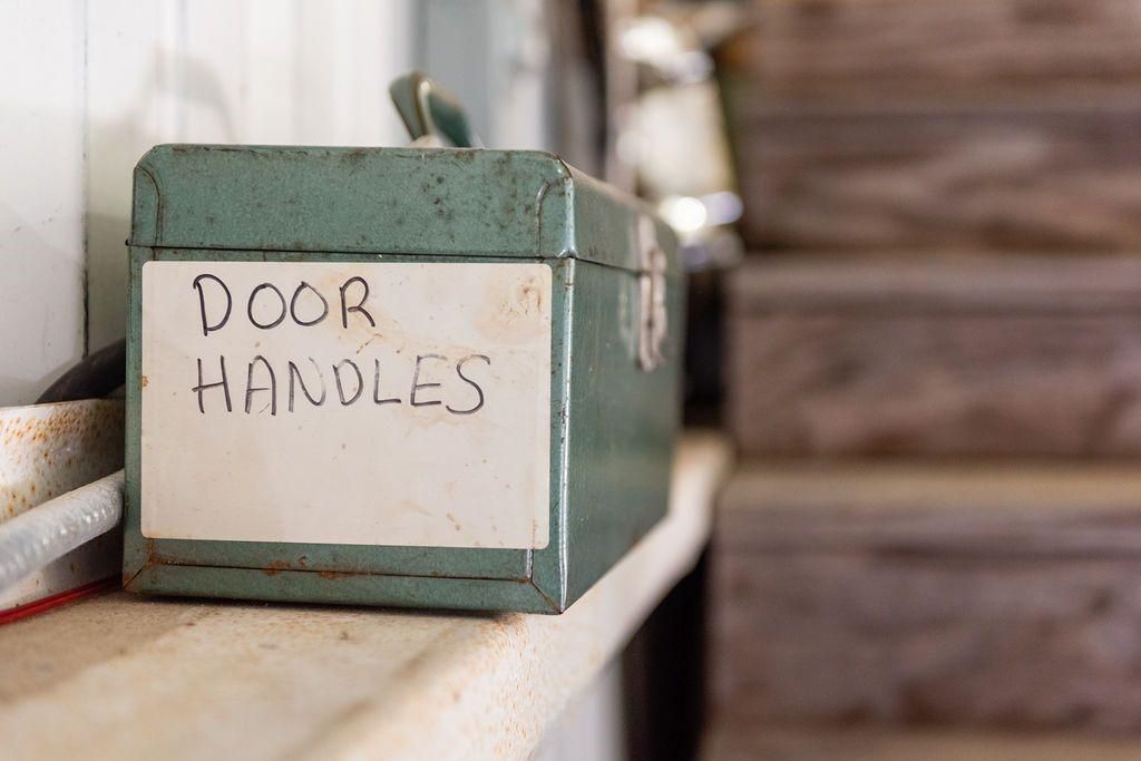 A green toolbox with a label that says `` door handles '' is sitting on a wooden shelf.