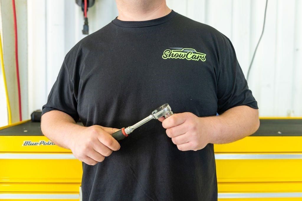 A man in a black shirt is holding a wrench.