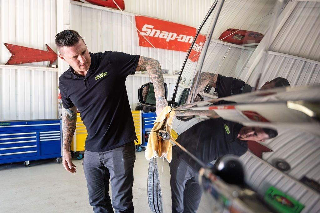 A man is cleaning a car in a garage with a snap on sign in the background.