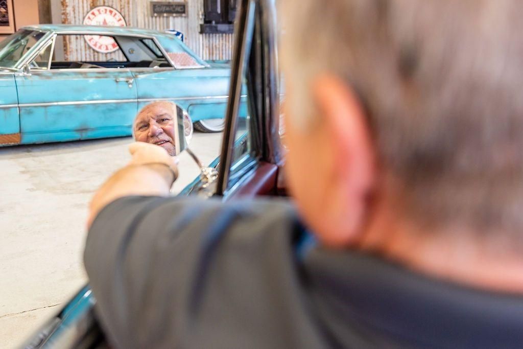 A man is looking at his reflection in a car mirror.