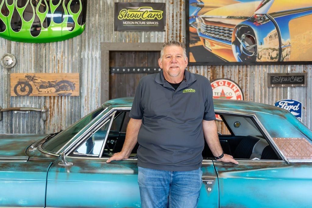 A man is standing next to a blue car in a garage.