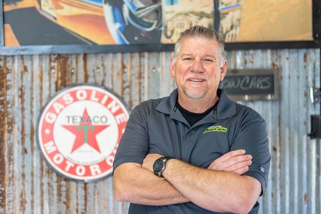 A man is standing with his arms crossed in front of a texaco sign.