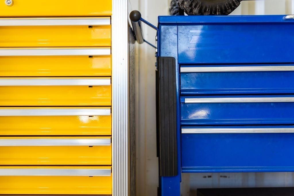A blue toolbox is next to a yellow toolbox in a garage.