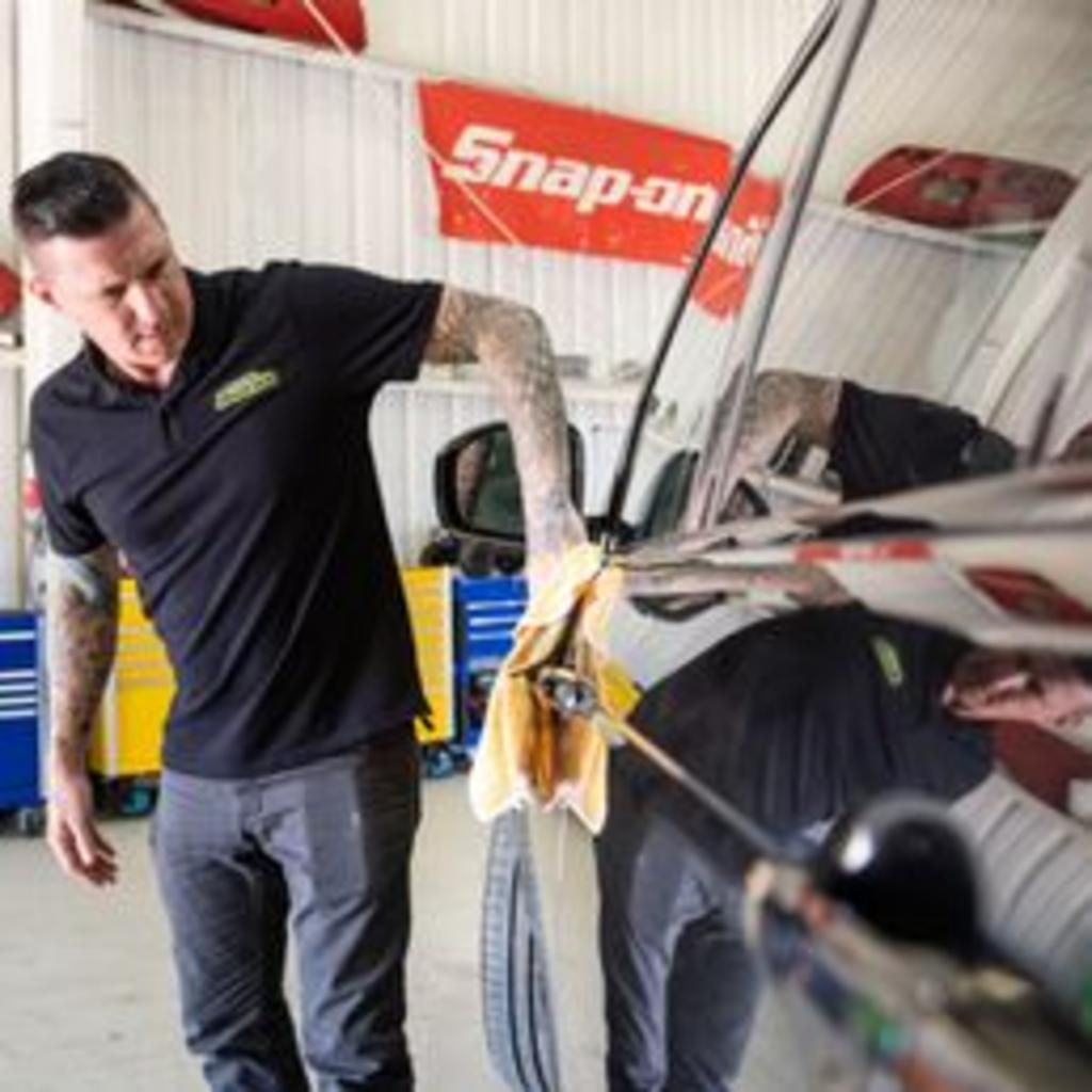 A man is cleaning a car with a towel in a garage.