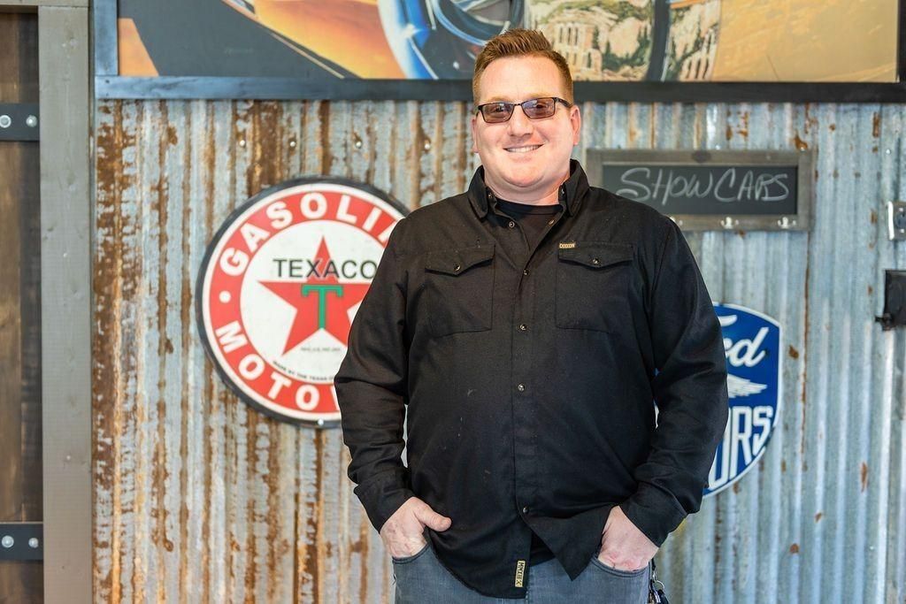 A man in a black jacket is standing in front of a sign that says gasoline.