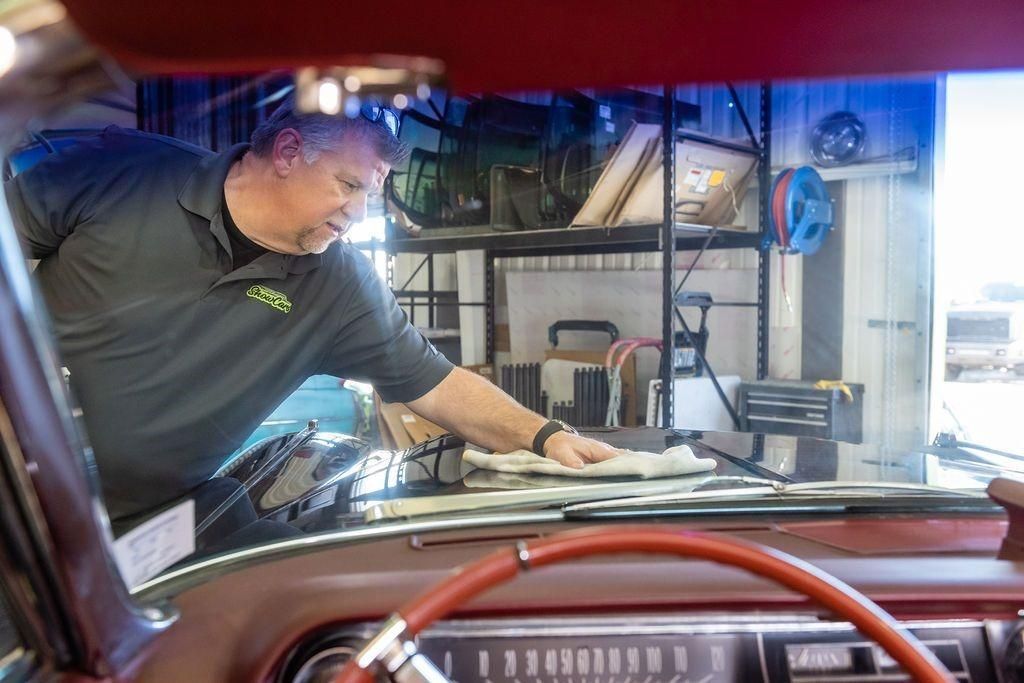A man is cleaning the windshield of a car in a garage.