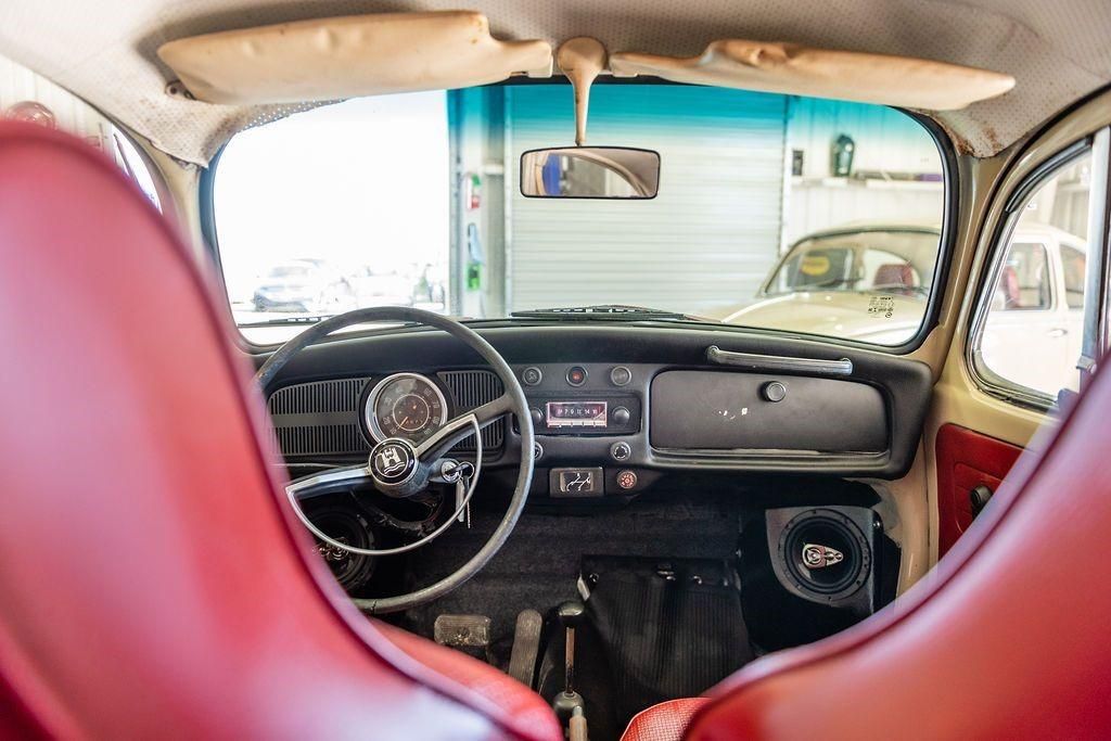 The inside of an old car with red seats and a steering wheel.