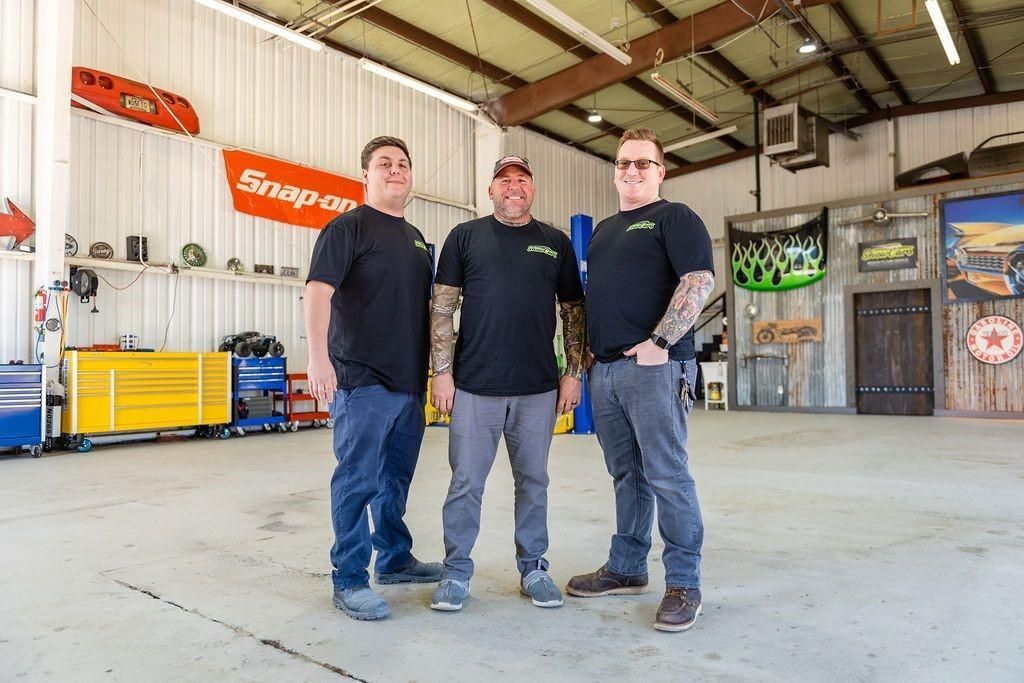 Three men are standing next to each other in a garage.