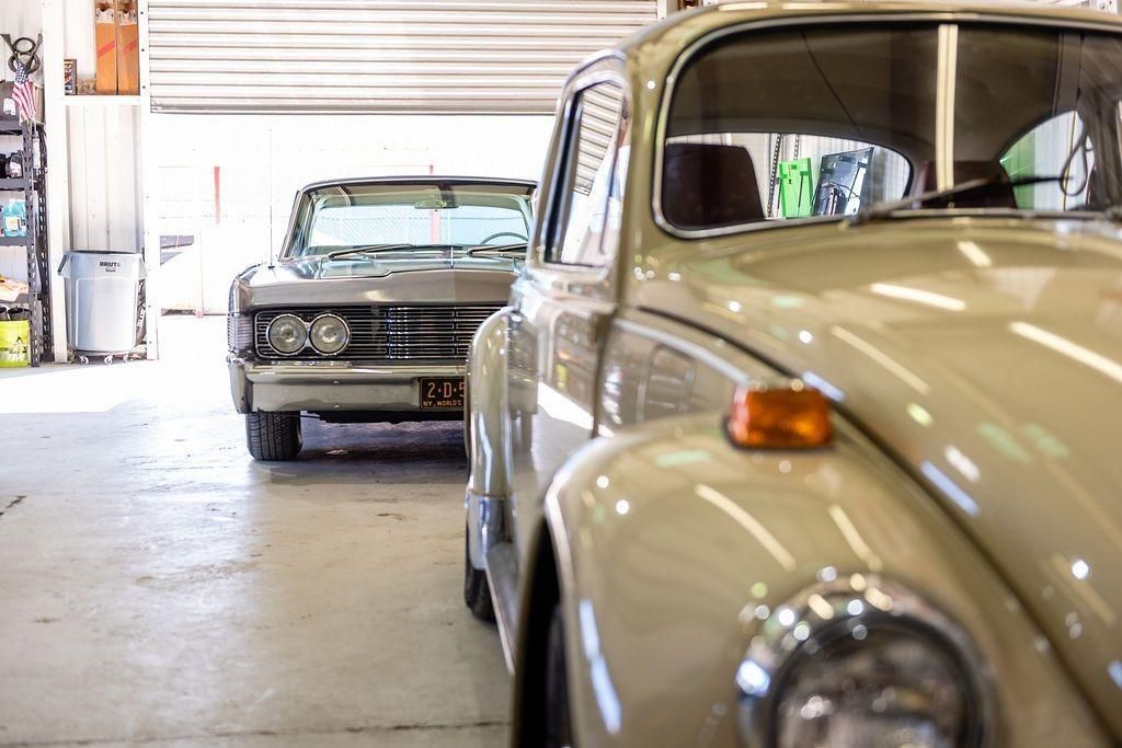 Two old cars are parked in a garage next to each other.