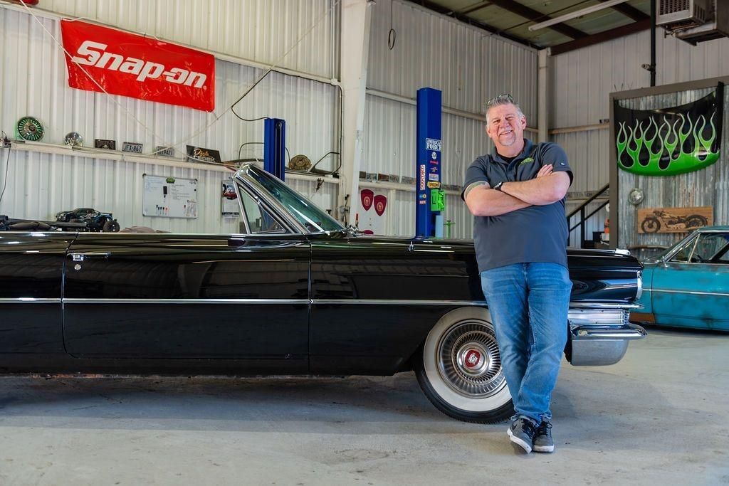 A man is standing next to a black car in a garage.
