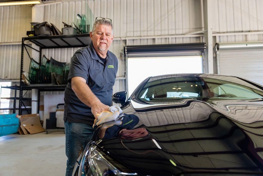 A man is standing next to a black car in a garage.