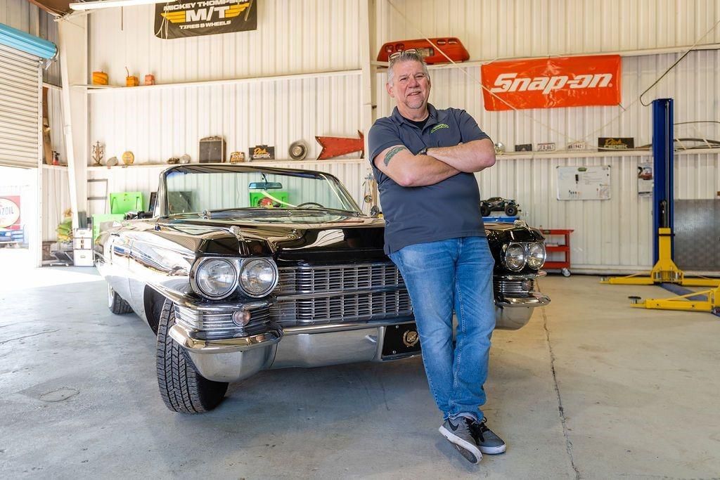 A man is leaning against a car in a garage.
