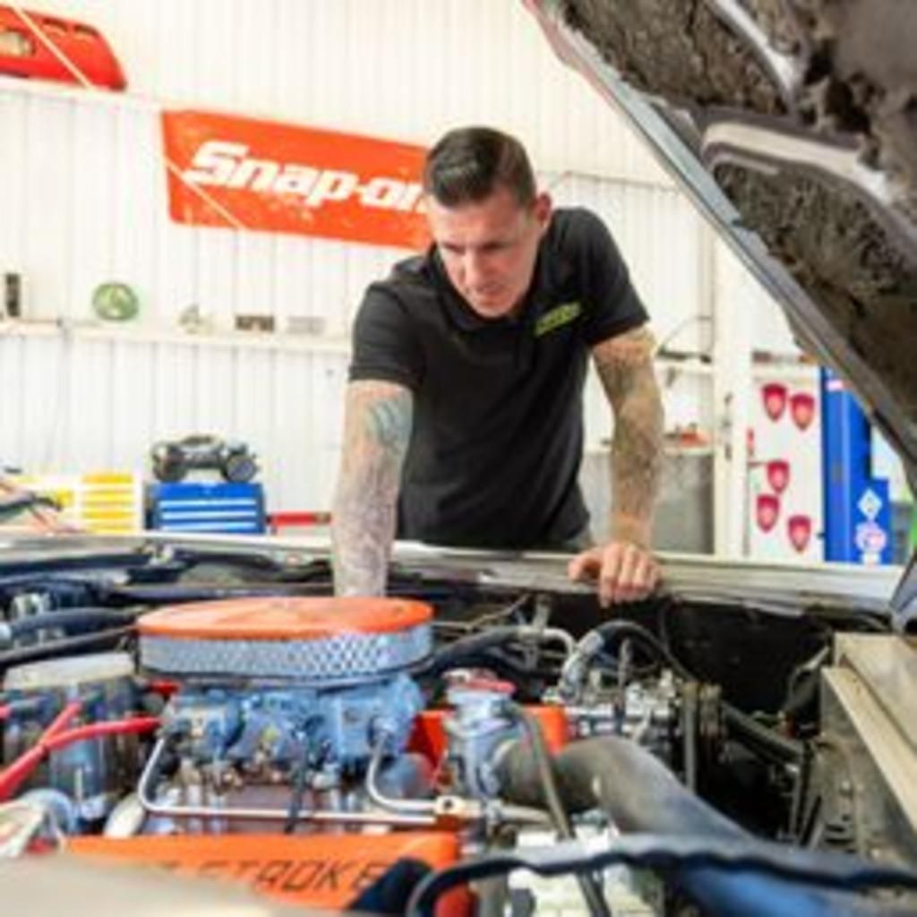 A man is working on a car engine with the hood open.
