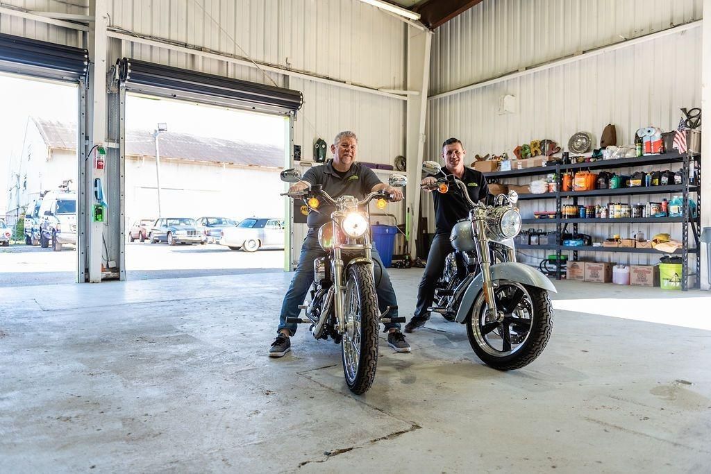 Two men are standing next to each other on motorcycles in a garage.