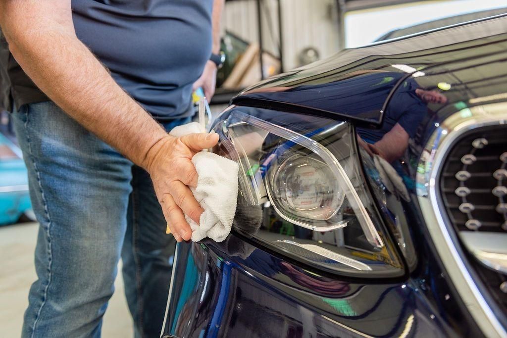 A man is cleaning the headlight of a car with a cloth.